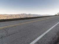 a road that has a side ramp on it with mountains in the background and a lone dog laying on the sidewalk next to it