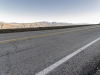 a road that has a side ramp on it with mountains in the background and a lone dog laying on the sidewalk next to it