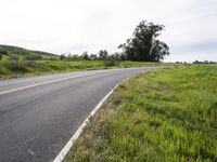 a black motorcycle is going along the road in a green grassy field by the side of the road