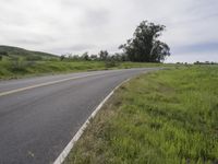 a black motorcycle is going along the road in a green grassy field by the side of the road