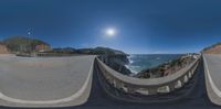 a 360 - view shows a curve on a highway by the ocean, near a rocky cliff and a body of water