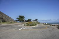 a stop sign near the ocean and an empty street by a grassy hill top on a clear day