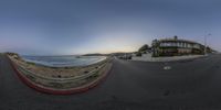 a wide angle view of a road in front of the ocean and a motel across from it