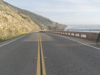 a view of the ocean from the side of a road near a coastline, with a photographer in the distance taking pictures