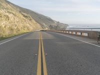 a view of the ocean from the side of a road near a coastline, with a photographer in the distance taking pictures