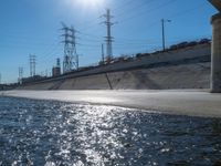 sun shining over a waterway on the side of a highway in california with power lines