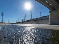 sun shining over a waterway on the side of a highway in california with power lines