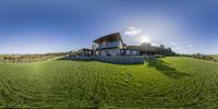 a house sits on the edge of a grassy hill in front of the sun shining