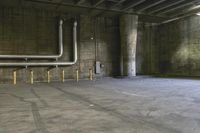 an empty industrial space with a bunch of pipes, benches and a parking lot inside