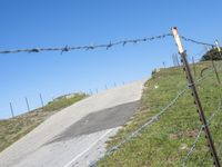 a barbed wire fence on a slope with two empty motorcycles parked nearby on the side