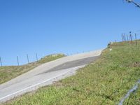 a person riding a motorcycle on a winding hill with barbed fence and blue sky in the background