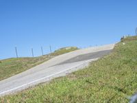 a person riding a motorcycle on a winding hill with barbed fence and blue sky in the background