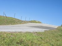 a person riding a motorcycle on a winding hill with barbed fence and blue sky in the background