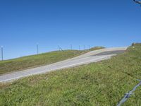 a person riding a motorcycle on a winding hill with barbed fence and blue sky in the background