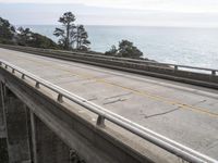 a truck crosses over the side of a bridge near the ocean and coastline in the distance