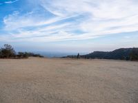 people at the top of a hill flying a kite in the air with mountains in the distance