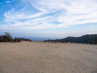 people at the top of a hill flying a kite in the air with mountains in the distance