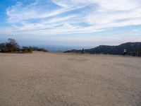 people at the top of a hill flying a kite in the air with mountains in the distance