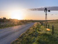 a country road at sunset with an old fashioned windmill in the distance, photographed in rural areas