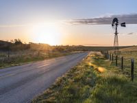 a country road at sunset with an old fashioned windmill in the distance, photographed in rural areas