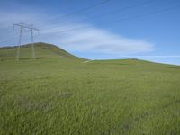 a farm with power lines above it on a grassy hill under blue skies and a power line in the distance