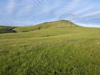 a farm with power lines above it on a grassy hill under blue skies and a power line in the distance