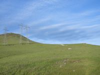 a farm with power lines above it on a grassy hill under blue skies and a power line in the distance