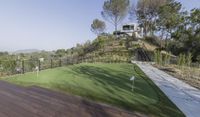 a house with large putting green on the side of a hillside with a golf course