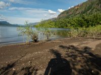 a person is standing in front of a lake on a sunny day, shadowing against the water and mountains