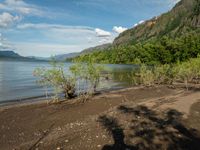 a person is standing in front of a lake on a sunny day, shadowing against the water and mountains