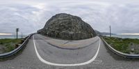 a car drives down a curved road near the ocean with a rock in the background