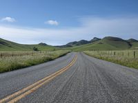 a road that has lines in the middle and mountains on both sides behind it, and blue skies above the horizon