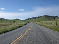 a road that has lines in the middle and mountains on both sides behind it, and blue skies above the horizon