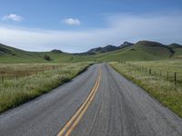 a road that has lines in the middle and mountains on both sides behind it, and blue skies above the horizon