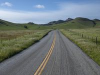 a road that has lines in the middle and mountains on both sides behind it, and blue skies above the horizon