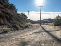 a dirt road with telephone poles on both sides of it and some hills on the other side