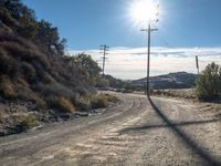 a dirt road with telephone poles on both sides of it and some hills on the other side