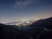 the view from the top of a mountain looking at city lights from the bottom of a hill