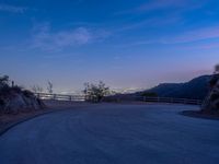 the moon rising over a valley and a road at dusk, with trees and fence surrounding it