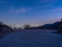 the moon rising over a valley and a road at dusk, with trees and fence surrounding it