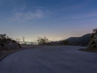 the moon rising over a valley and a road at dusk, with trees and fence surrounding it