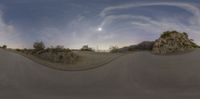 an old fashioned street with two large rocks and grass behind it and the sun going down in the sky and moon rising above