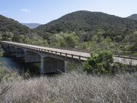 a view from a bridge overlooking trees and a mountain range of hills behind a bridge