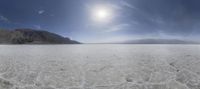 a wide open plain with clouds, rocks, mountains, and water below the sun