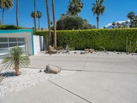 a planter and rocks are in the driveway by a green hedge and a white stucco house