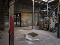 a fire hydrant in an old industrial setting in a factory building, with a lot of equipment, exposed ceilings and a cement floor