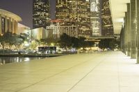 a long sidewalk near a body of water with tall buildings behind it at night time