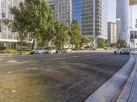 a street lined with cars, with tall buildings in the background, and green trees along side