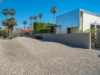 an empty driveway leading into a home with palm trees in the background, and a concrete wall in front of it