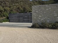 a brick wall with two sections of a concrete driveway and bushes in front of it